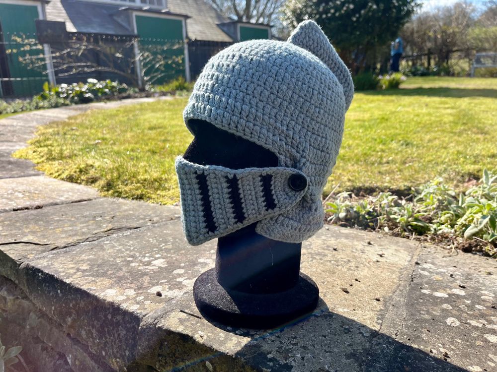A knitted knight helmet on a display head.