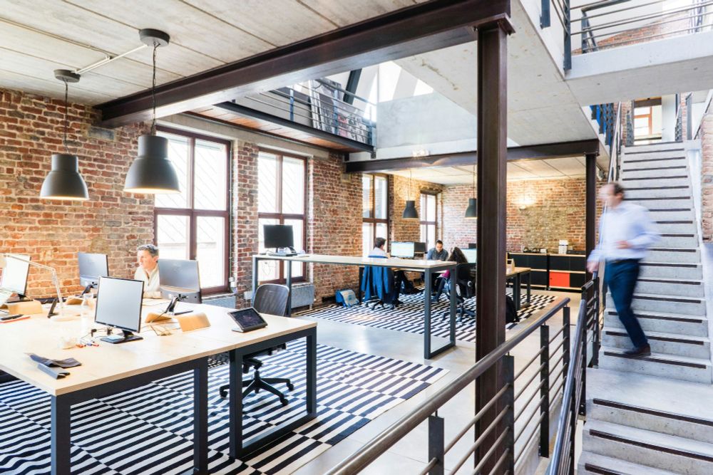 An industrial style open plan office with desks, computers, and large black ceiling lamps