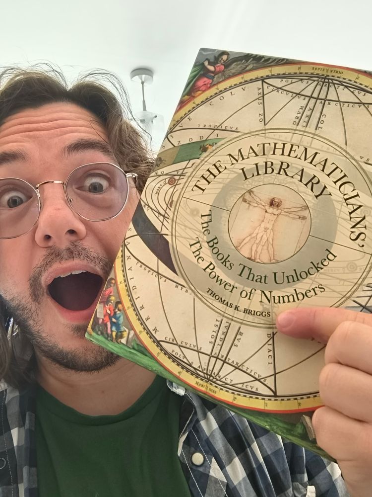 Me, a bespectacled, furry-faced man of 42, holding a book titled "The Mathematicians Library, The Books That Unlocked The Power of Numbers". My finger is pointing at the author's name, which is "Thomas K. Briggs". My face holds a look of shock and surprise.