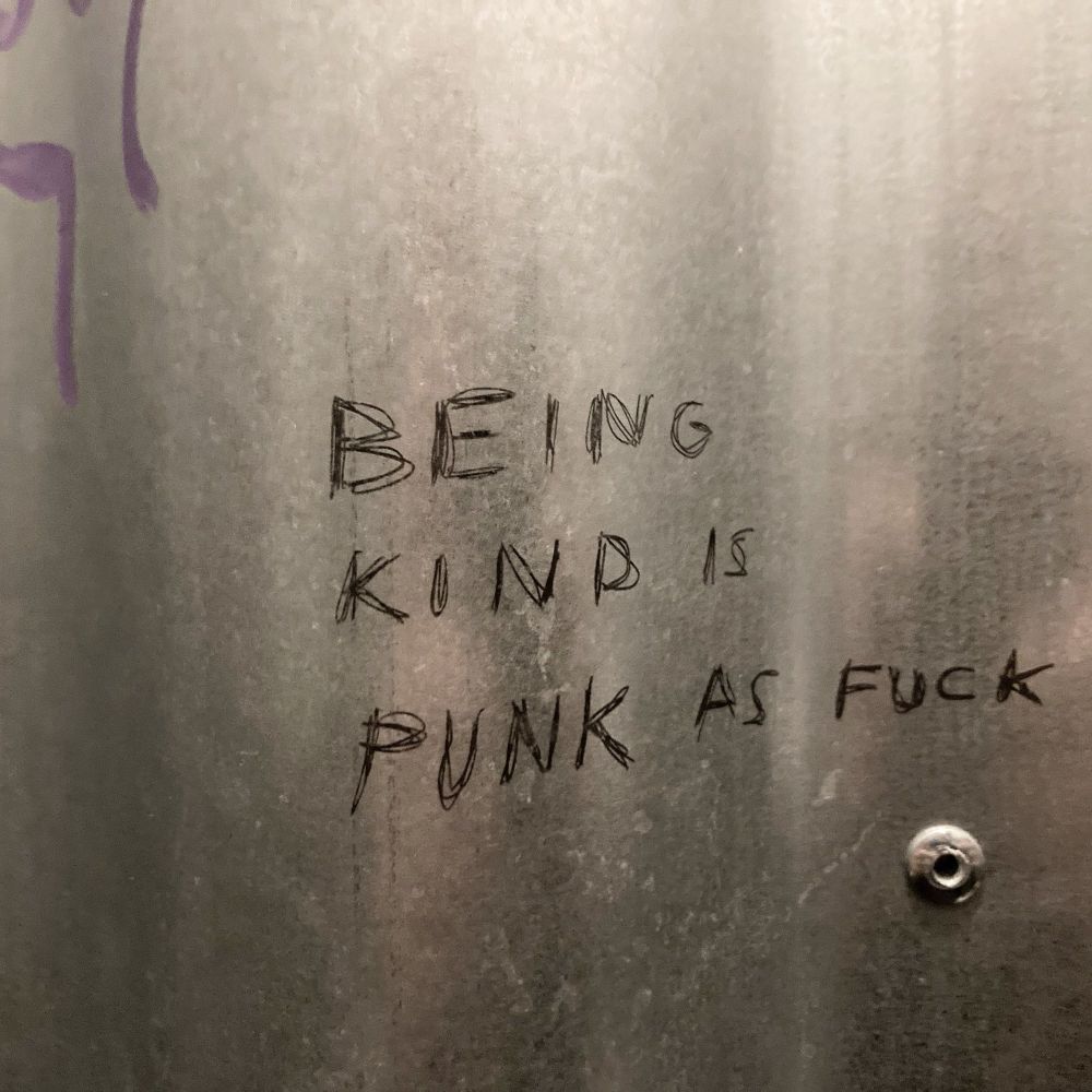 Metal plate wall with scratched inscription of BEING KIND IS PUNK AS FUCK.