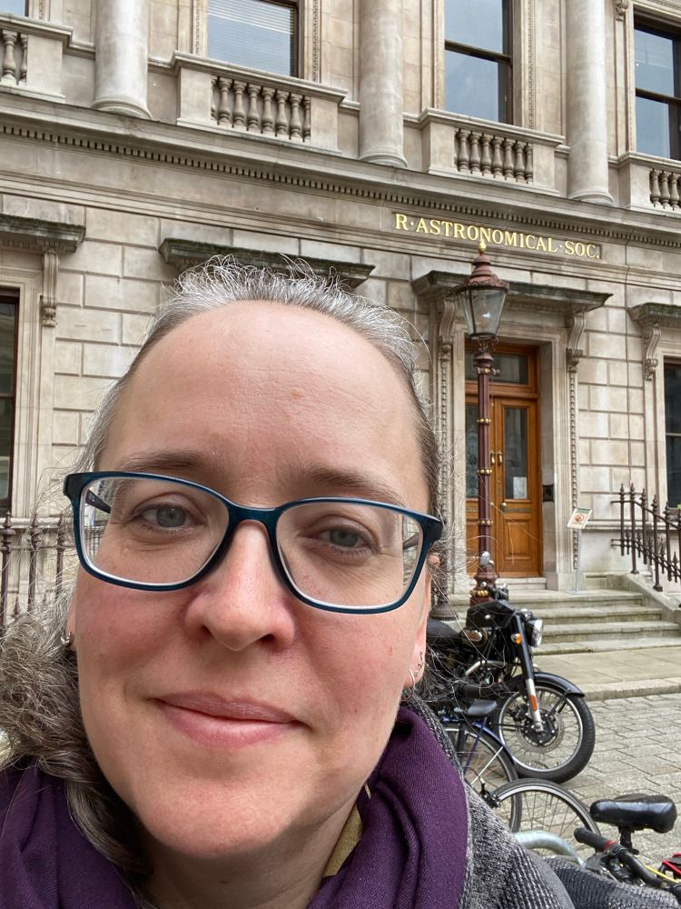 A woman in front of a stone building with the label “R. Astronomical Soc.” 