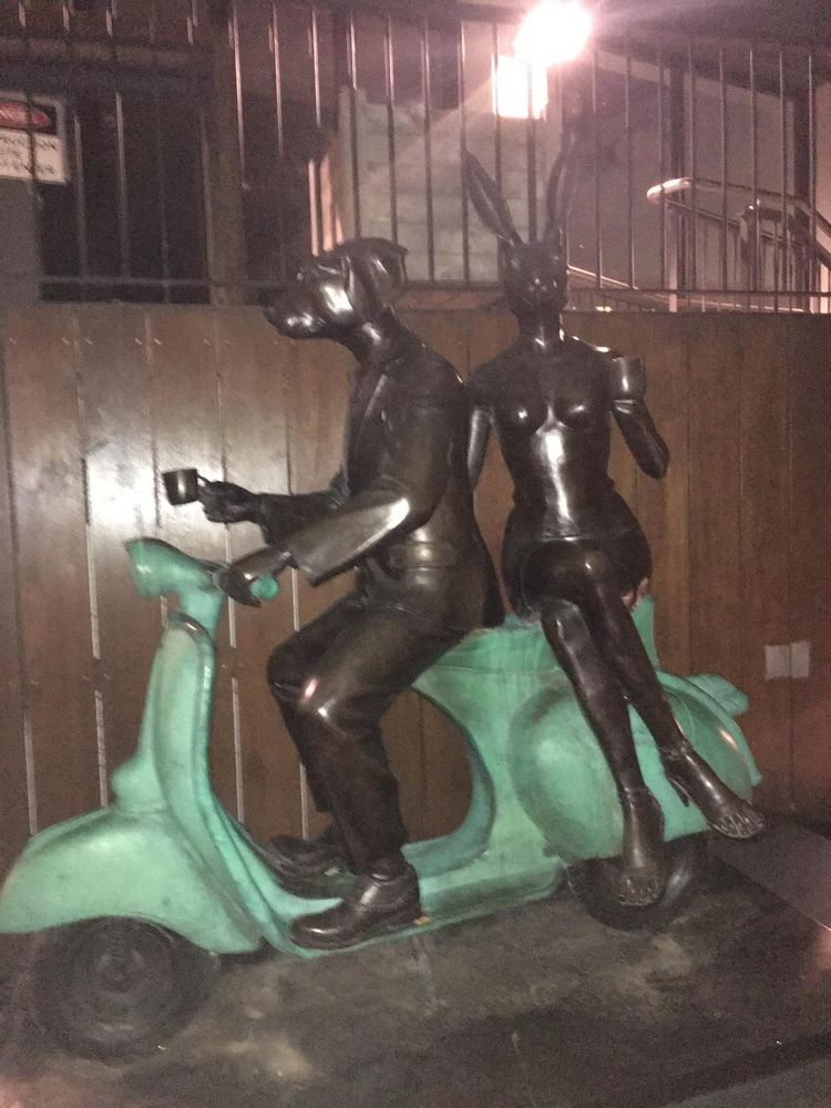 Statue of an anthropomorphised male dog in a suit and female rabbit in a dress and heels holding cups riding a Vespa. I really have no idea what this is meant to represent. 