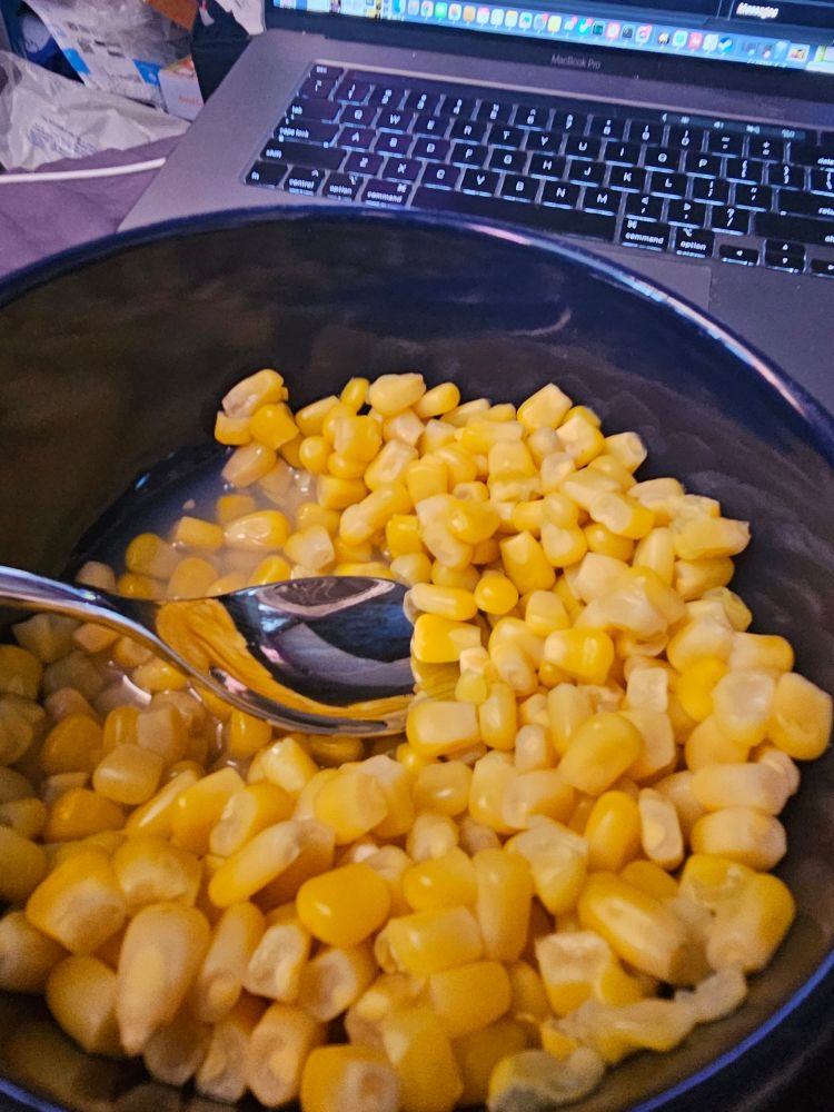 a bowl of cooked canned corn with a spoon in it