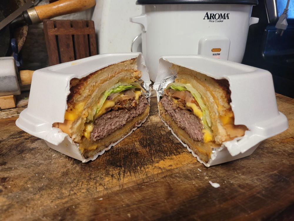 The Big Aristotle burger from Big Shot Bob's in Pittsburgh, cleanly sliced in half, still inside its container and foil, which is also cleanly sliced in half.