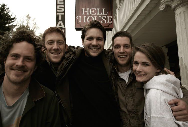 Five friends standing outside their haunted property and smiling. 