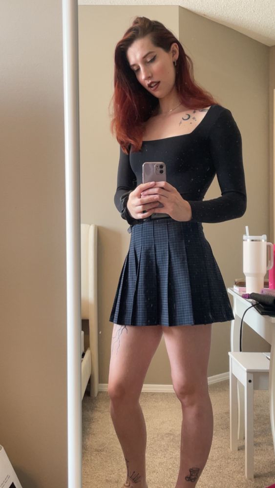 girlbossify in black bodysuit and navy skirt posing in the mirror