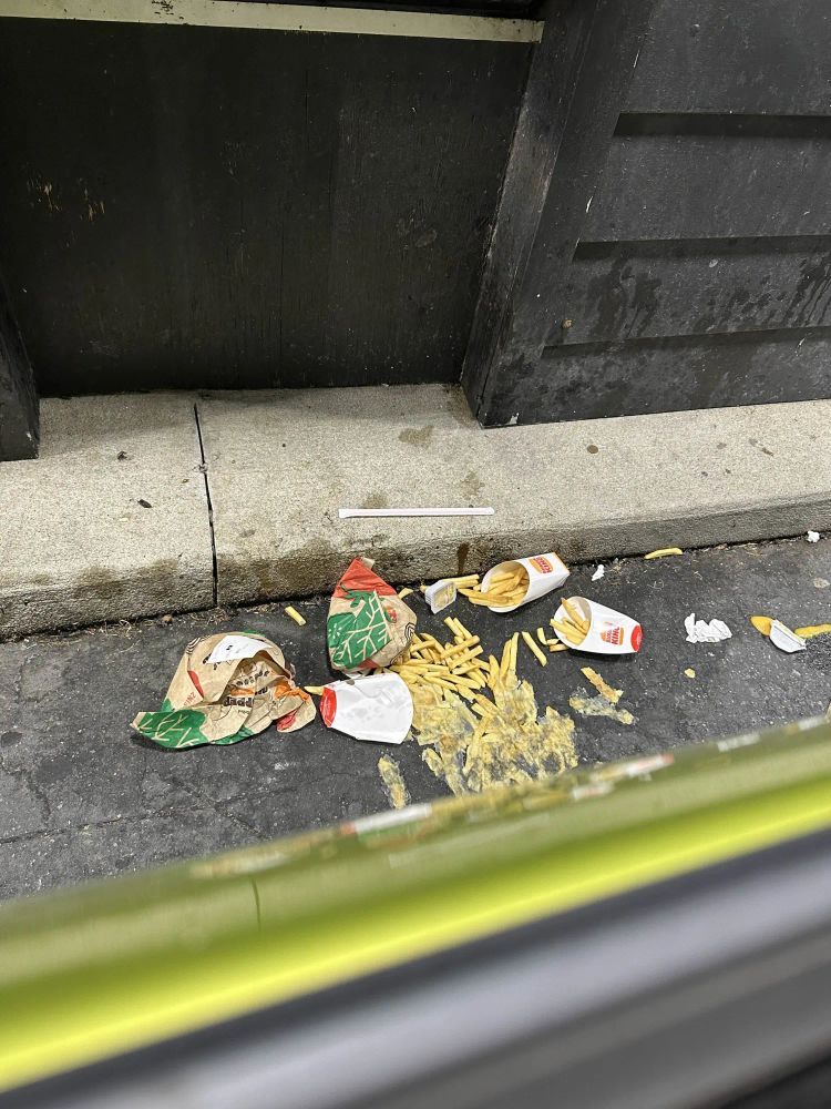 picture of 2 large burger king combo meals fallen and discarded on the floor. Some of the french fries have been squashed under the tires of a car.