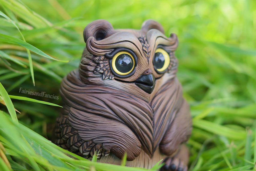 Photo of a sculpture about 5 inches tall of a baby version of the d and d owl bear sitting in the grass. Eyes are wide and expression seems as if this creature doesn’t know it exists yet. No brain cells.  