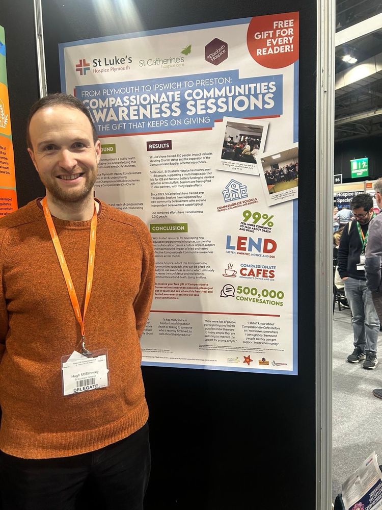 Man with brown jumper and orange lanyard in front of conference poster on Compassionate Communities