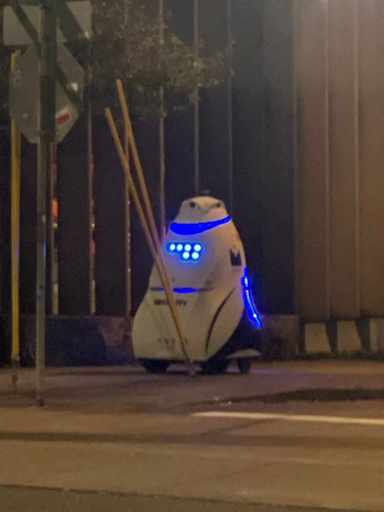 a white robot with blue lights on a side walk at night 