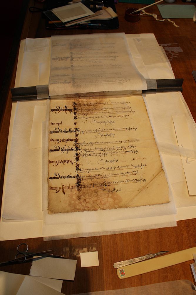 The document rests on a table surrounded by the conservators' tools and equipment. There are no illustrations. The document is made of paper.