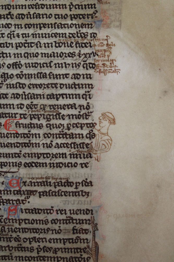 A monk in brown ink has been drawn in a legal manuscript pointing at an important sentence in the right hand column of text on the page. The artist has only drawn his head and torso. He has a a tonsure and is shown in profile.