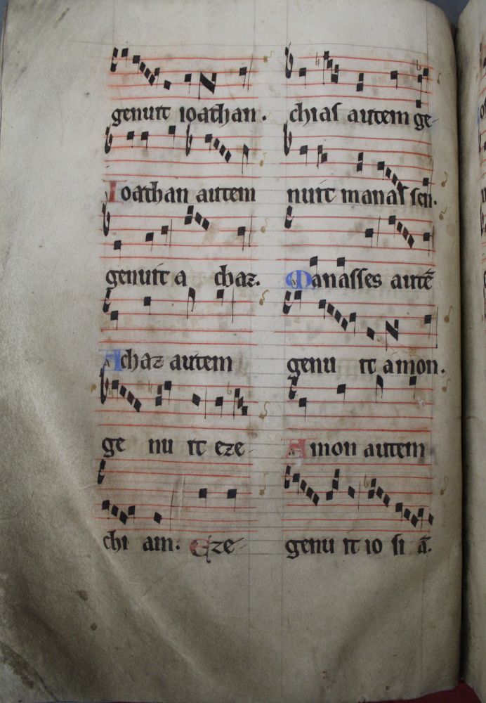 Two columns of music are on the page. Each column  has 6 parts. The top five parts are staves of 5 lines. The last part has a stave of 6 lines. The musical notes have been drawn as black squares with tails. Red or Blue capital letters are given for names. The lines are in red.