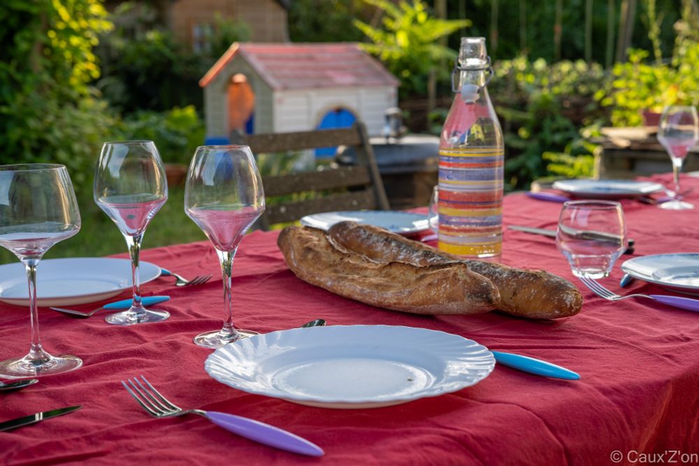 Sur une table nappée de rouge est dressée une table, des couverts et des verres. On y aperçoit deux baguettes et une bouteille d'eau 