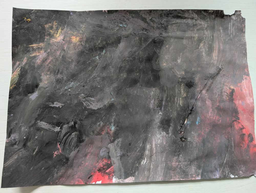 Ein A4-Blatt im Querformat bemalt mit schwarzer Wasserfarbe. Es schimmert etwas Rot, Blau und Gelb durch.