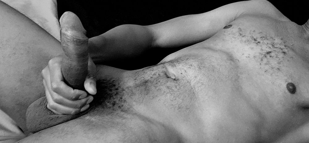 A black and white body pic of Jay laying down naked holding his erection