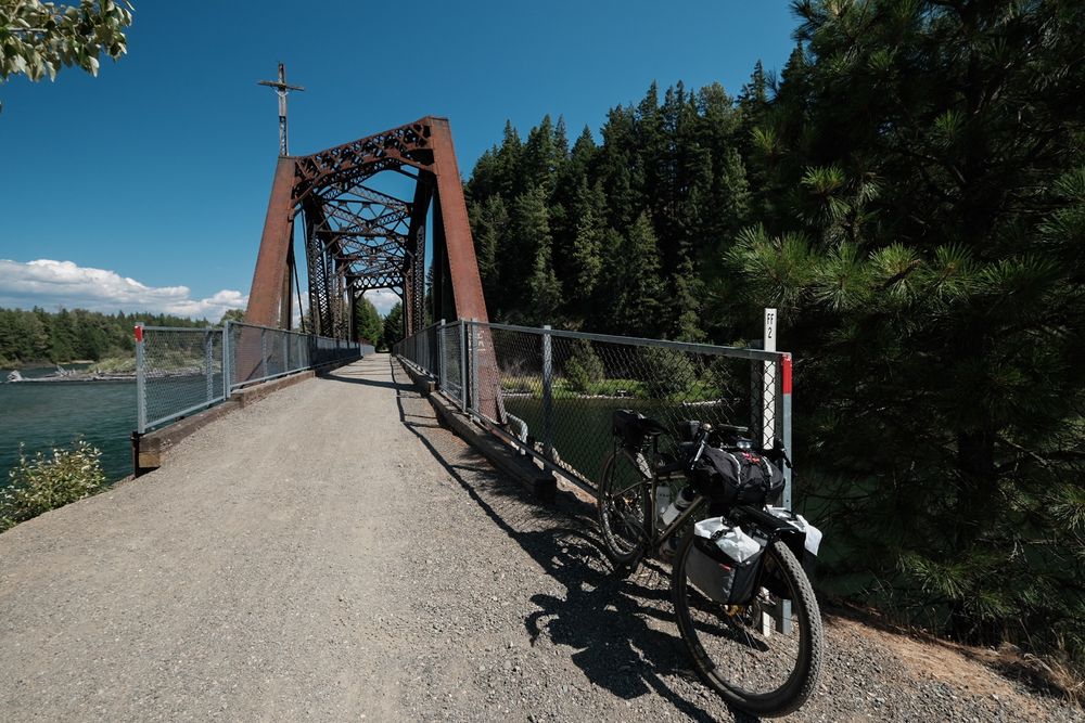A bikepacking bike (Kona Sutra LTD) is facing the camera and an old train trestle crossing the Yakima River is in the back.