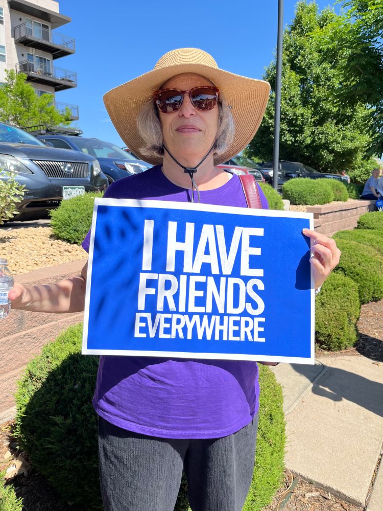 a woman carrying a sign that says, "I have friends everywhere," a code phrase for identifying people in the Resistance in ANDOR