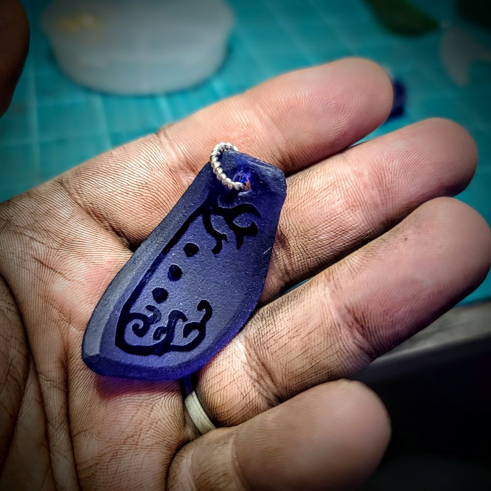 hand holding a piece of blue sea glass etched withvine like lines