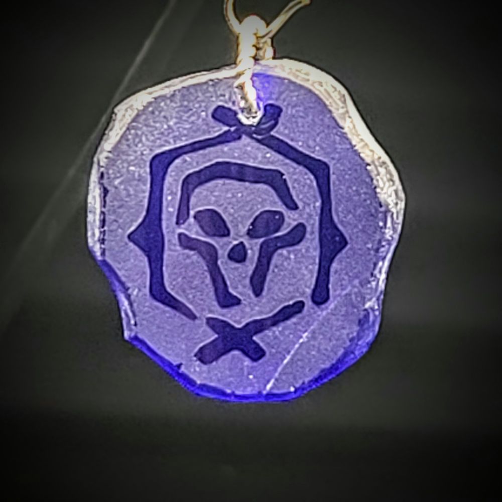 chunk of blue sea glass pendant with an athenias fortune logo from the game sea of thieves