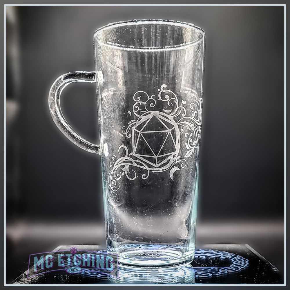 a tall coffee mug etched with a d20 gaming dice and filigree design