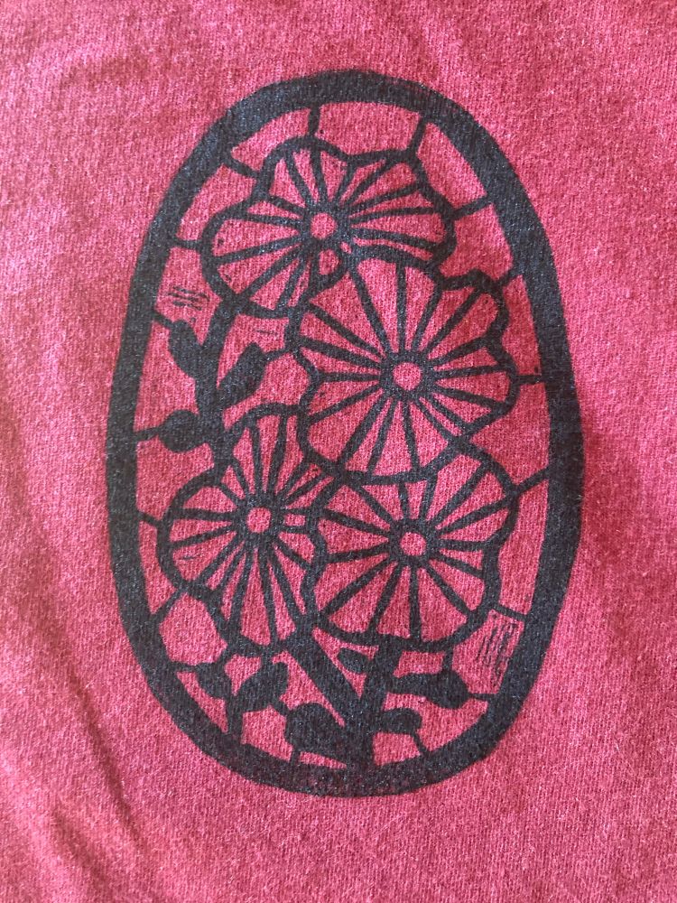 An oval shaped stained-glass-style stamp, depicting stripey flowers with thick black stalks, printed with black ink on a red sweatshirt.