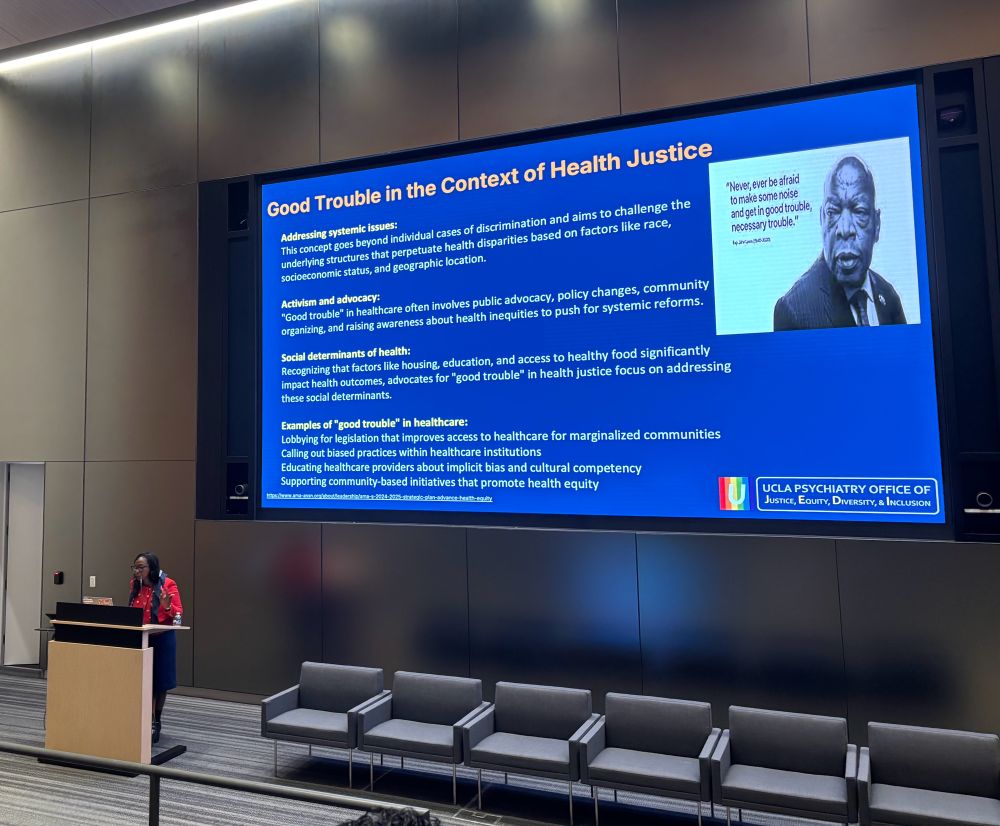 Dr Bath presenting in the pritzker auditorium in front of a slide on good trouble in the context of health justice 