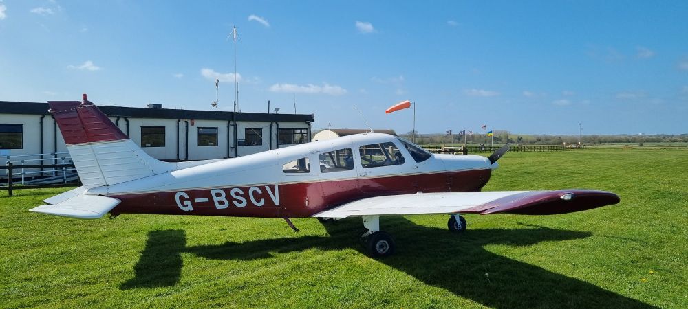 Piper PA28 parked outside the club house at Old Buckenham Airfield in Norfolk. The windsock in the background showing quite a wind!  300 @ 26kts as we joined the circuit (for runway 25) but thankfully dropped to 13kts on final 😄 