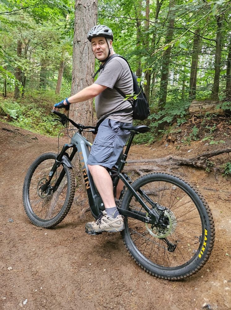 Man stood over a large mountain bike, mid ride through a forest