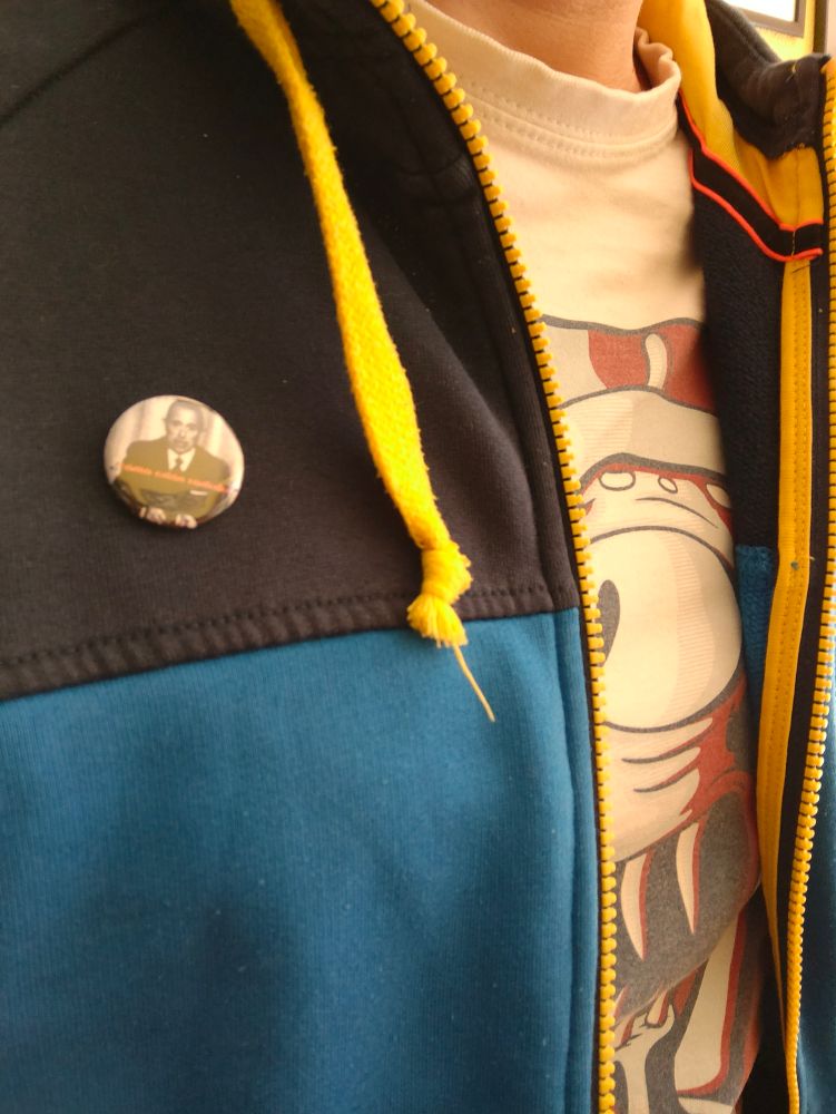 Foto de servidor con una sudadera donde se ve una chapa. Bajo la sudadera, una camiseta con el retrato de Kang modo Obama. 