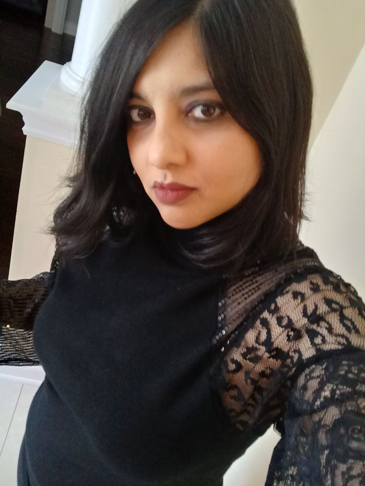 A picture of me, a brown woman, In a black shirt with lace sleeves. 