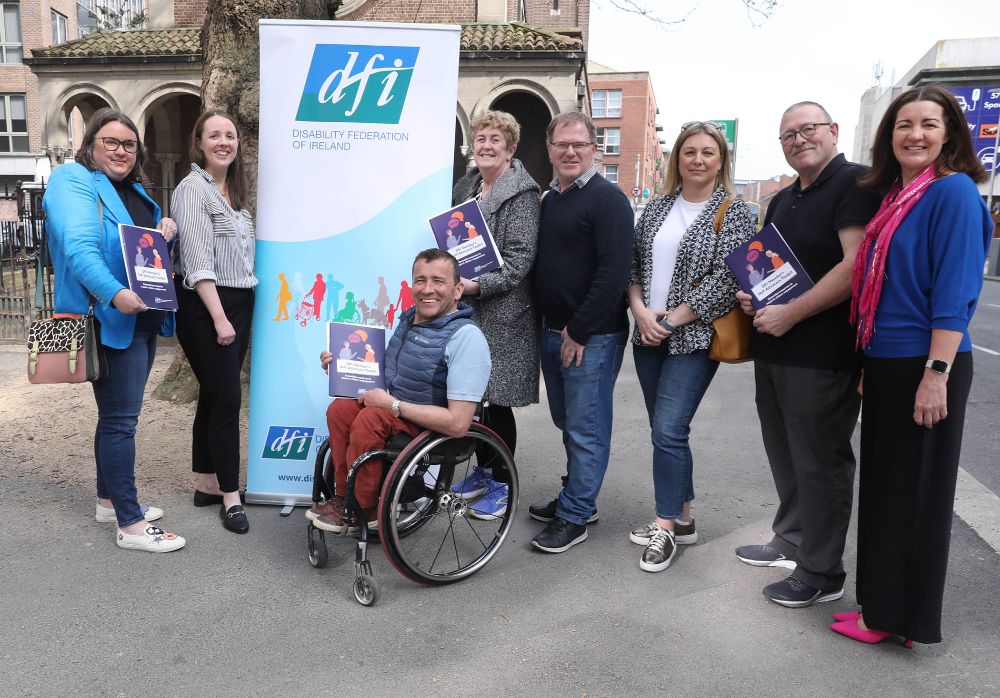8 people in front of a DFI pop-up banner holding copies of DFI's Self-Advocacy Toolkit.