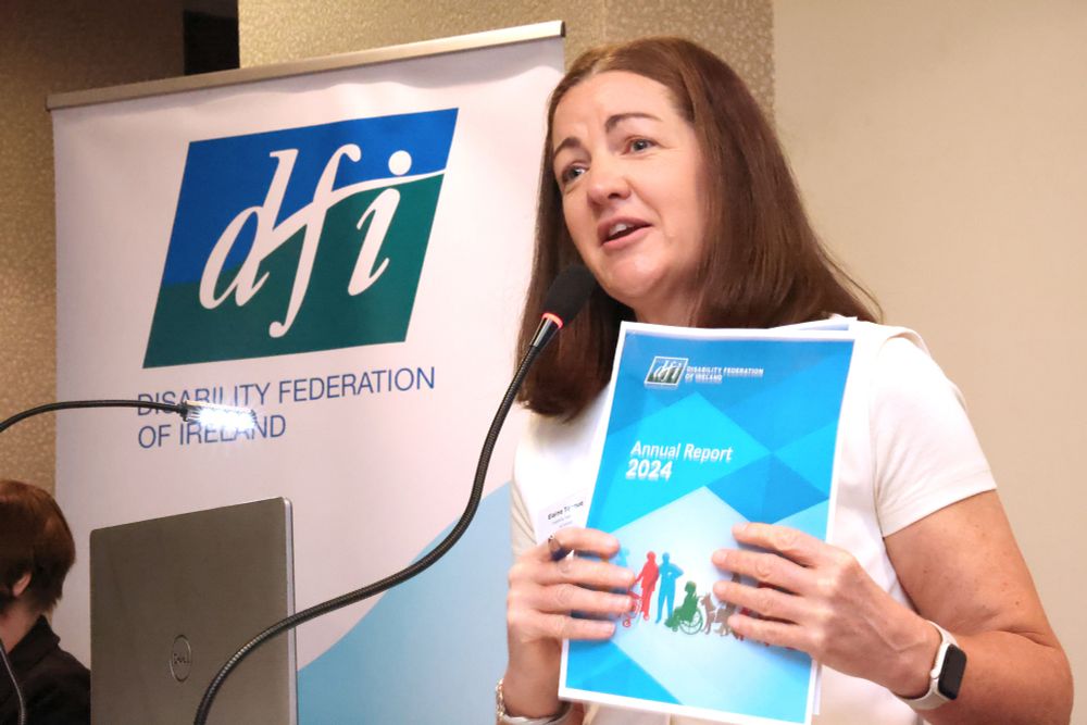 A speaker at a podium holding the 2024 DFI Annual Report in front of a DFI banner.
