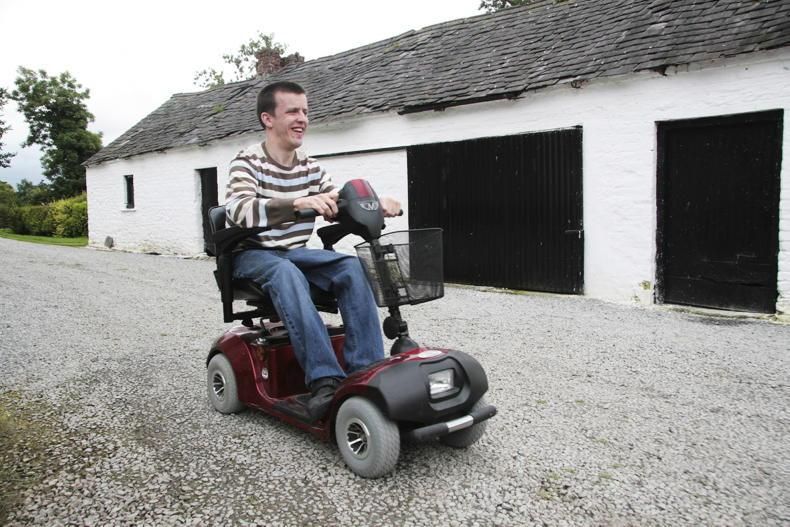 A man in a motorised wheelchair on a rural road.