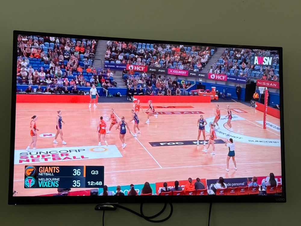 Television on the wall showing awsn.tv with an Australian instance of a Netball match