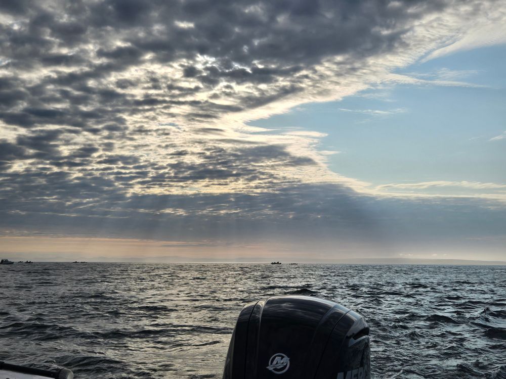 Photos of light rays breaking through morning clouds over the ocean with a boat motor in view.