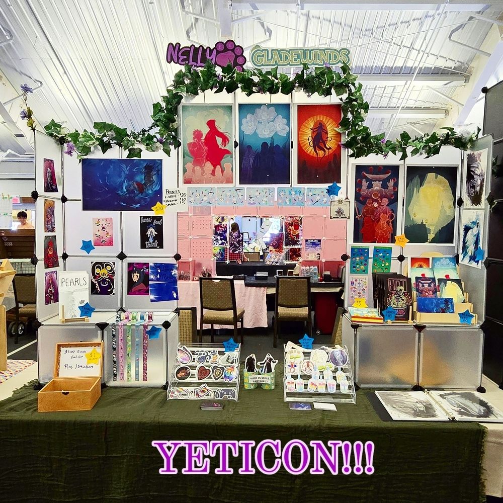 Photo of convention table with prints and stickers in bright colours with 'YETICON!!!!' Acroas the bottom I purple font.