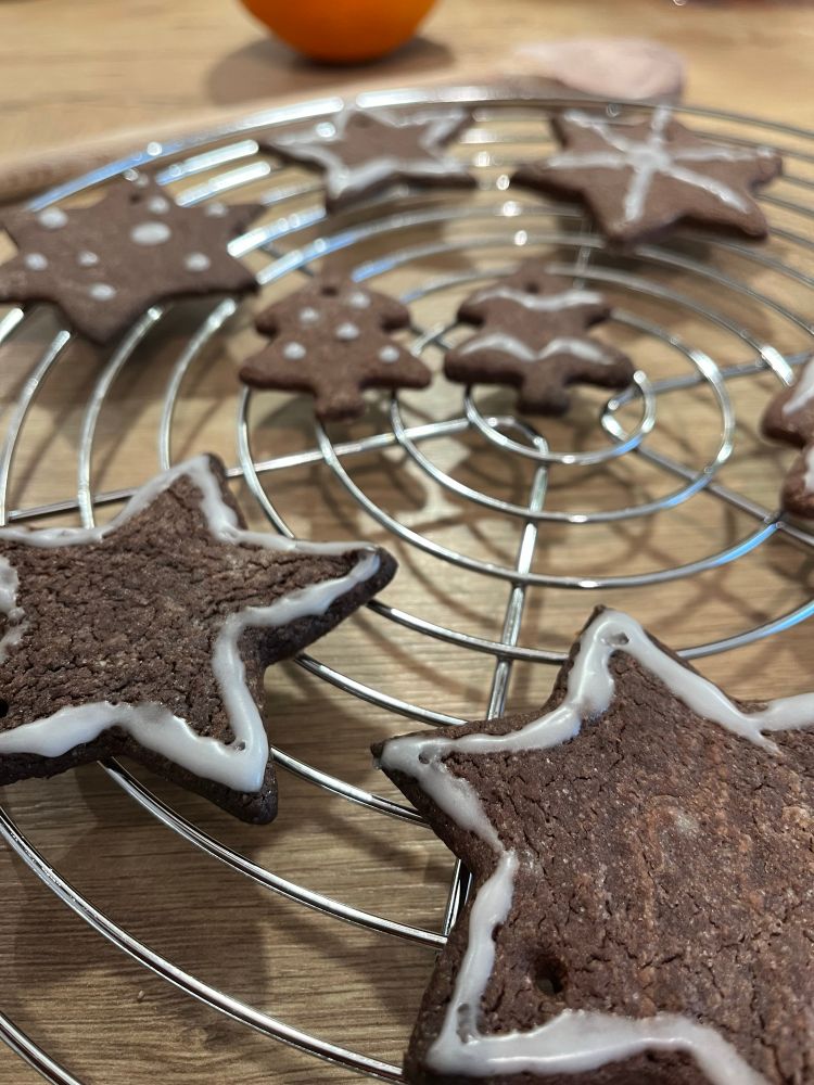 Chocolate cookies in the shape of stars and Christmas trees, baked and decorated by yours truly, cooling on a rack 