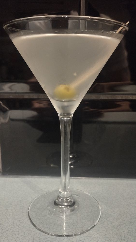 A Dirty Martini cocktail in a Martini glass, garnished with a green olive on a cocktail stick.