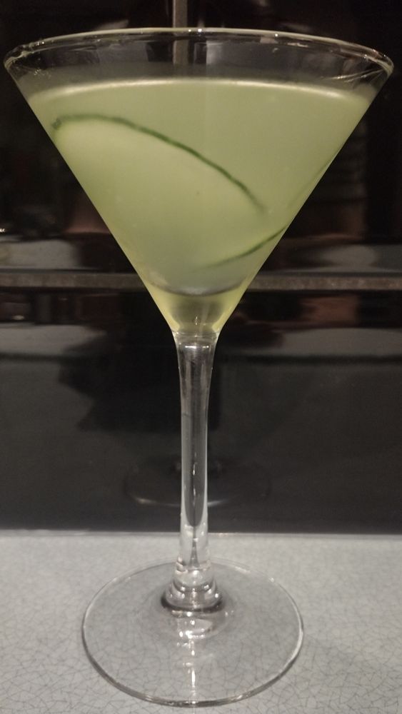 A green-tinged Cucumber Martini in a cocktail glass, garnished with thin slices of cucumber floating in the drink.