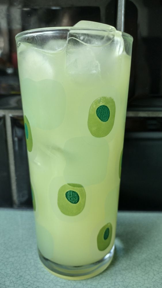 A cloudy green Mauresque cocktail in a tall ice-filled glass that is decorated with green shapes.