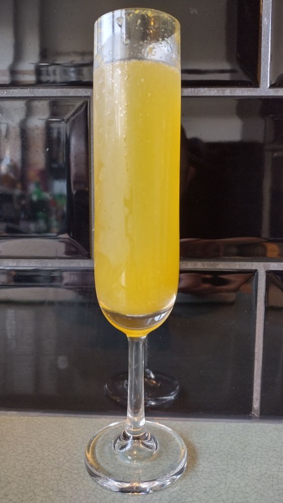 A champagne flute filled with orange-coloured Buck's Fizz.