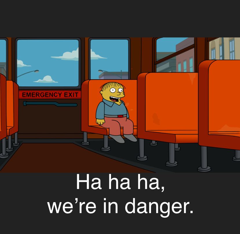 Ralph Wiggum sits in the last row of an empty school bus, smiling. A caption beneath him displays the words he is speaking: “Ha ha ha, we’re in danger.”