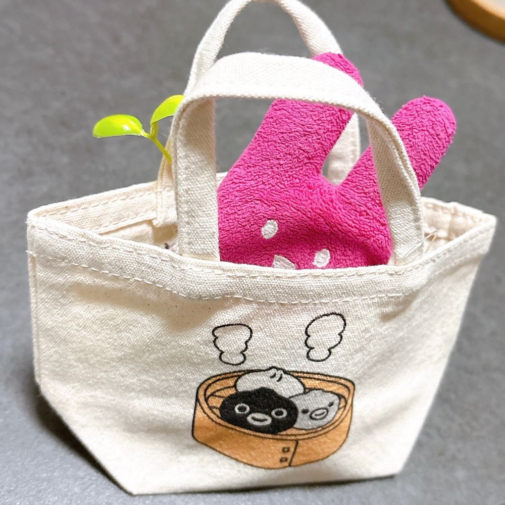 手のひらサイズのミニトートバッグと、その中に入っているばにちゃ。トートバッグにはせいろで蒸されるスイカペンギンが描かれている
