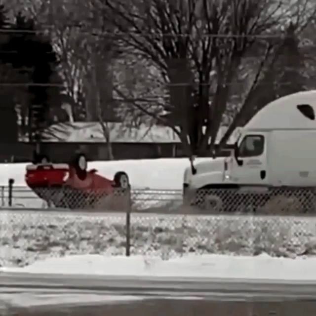 a white semi truck is driving down a snowy road next to a red car that is on the side of the road .