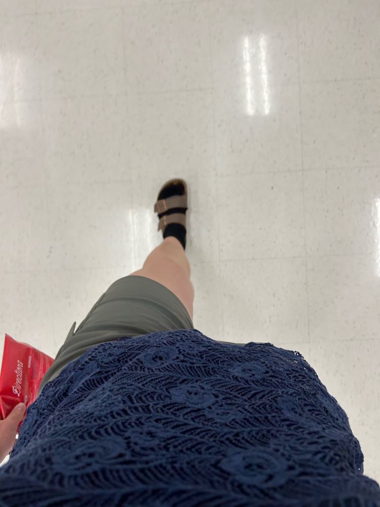 a photo from first-person perspective, looking down at the person’s feet mid-step. she’s wearing Birkenstock sandals, black socks, green shorts and a blue shirt.