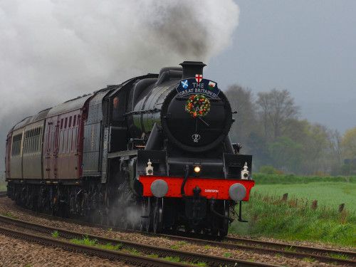 Steam train travelling alongside green fields. Image credit: The Great Britain Steam Train. Photo by Christopher More on Pexels. https://www.pexels.com/photo/the-great-britain-steam-train-17396360/. 