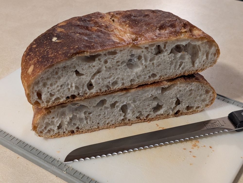 The round sourdough bread loaf has been cut in half to display the inner crumb. It is spongy and delicious.