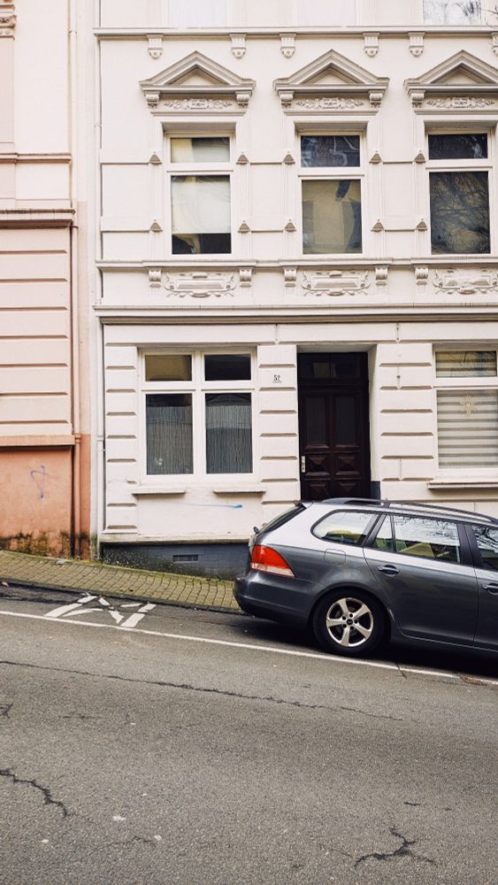 Ein Auto steht an einer sehr steilen Straße vor einem Haus. 
