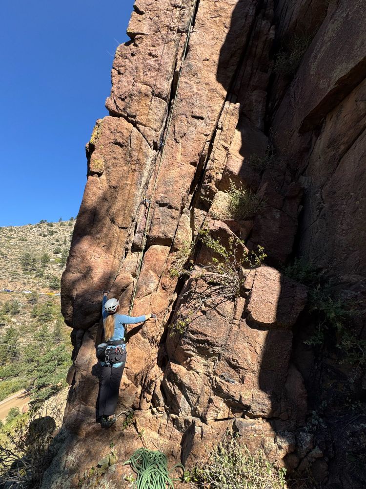 Rock climber in a blue sun shirt at the base of a hand crack, both hands on the rock. 🧗